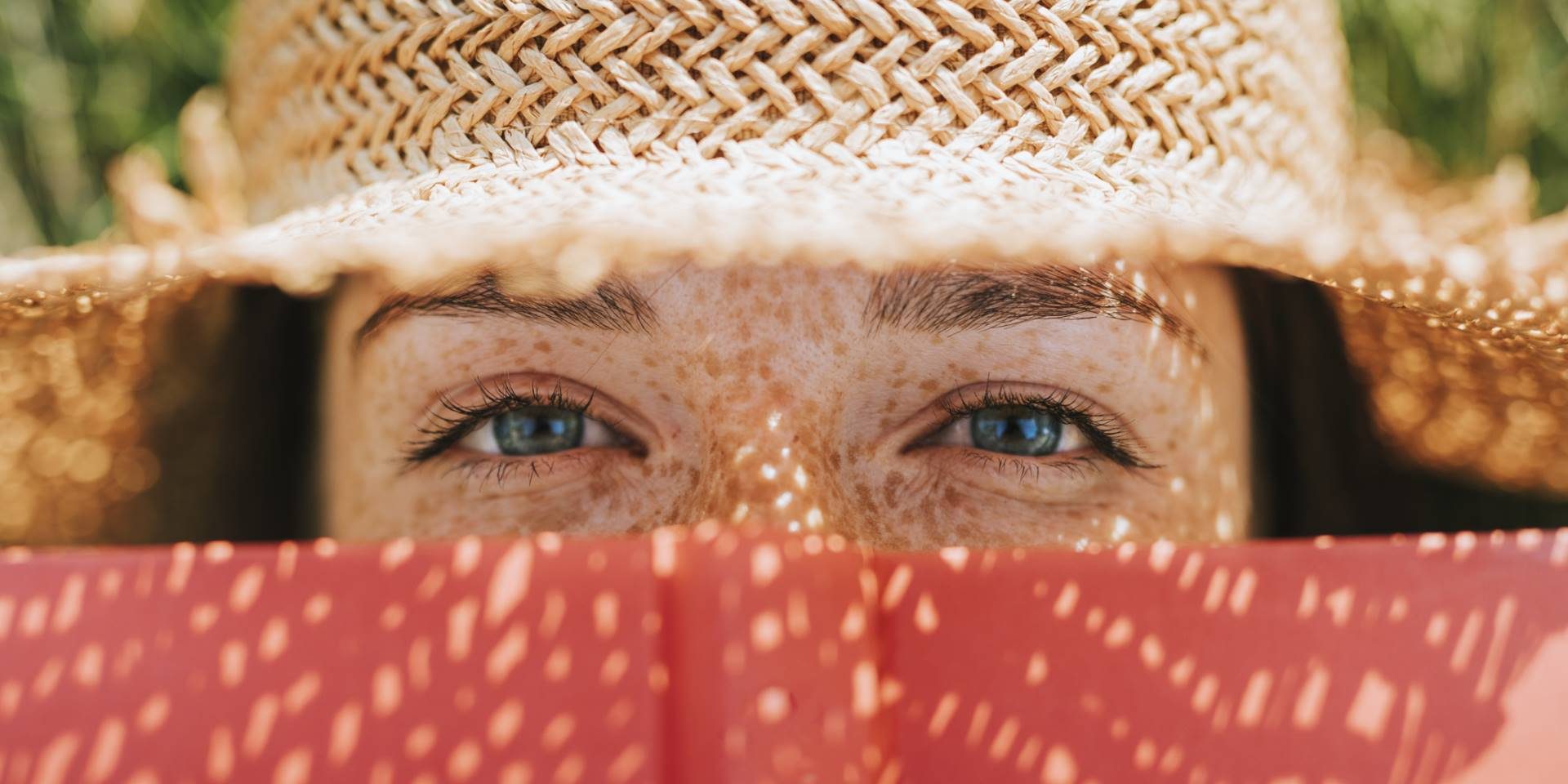 Closeup of woman covering her face with a red book